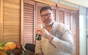 Jono sits at a kitchen table and holds a mixer containing AG1 supplement.