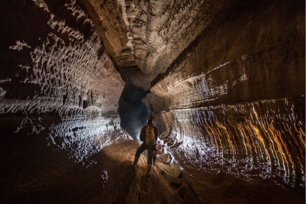 An image from inside the Armageddon cave system, showing a caver standing in  in a high and wide chamber.