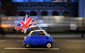 A man waves Union flags from a BMW Isetta as he drives past Brexit supporters gathering in Parliament Square, in central London on January 31, 2020, the day that the UK formally leaves the European Union