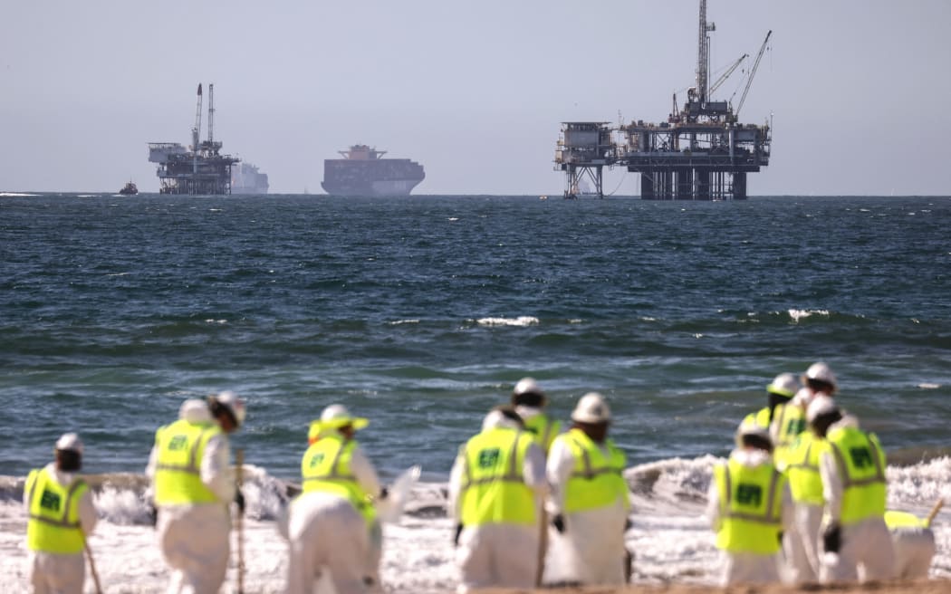 HUNTINGTON BEACH, CALIFORNIA - OCTOBER 09: Cleanup workers search for contaminated sand and seaweed in front of drilling platforms and container ships about one week after an oil spill from an offshore oil platform on October 9, 2021 in Huntington Beach, California. The heavy crude oil spill affected close to 25 miles of coastline in Orange County. Huntington Beach is open but the public is not allowed to enter the water.   Mario Tama/Getty Images/AFP (Photo by MARIO TAMA / GETTY IMAGES NORTH AMERICA / Getty Images via AFP)