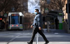 A man crosses an empty street in Melbourne on 23 August 2021, as the city experiences its sixth lockdown while battling an outbreak of the Delta variant of coronavirus.