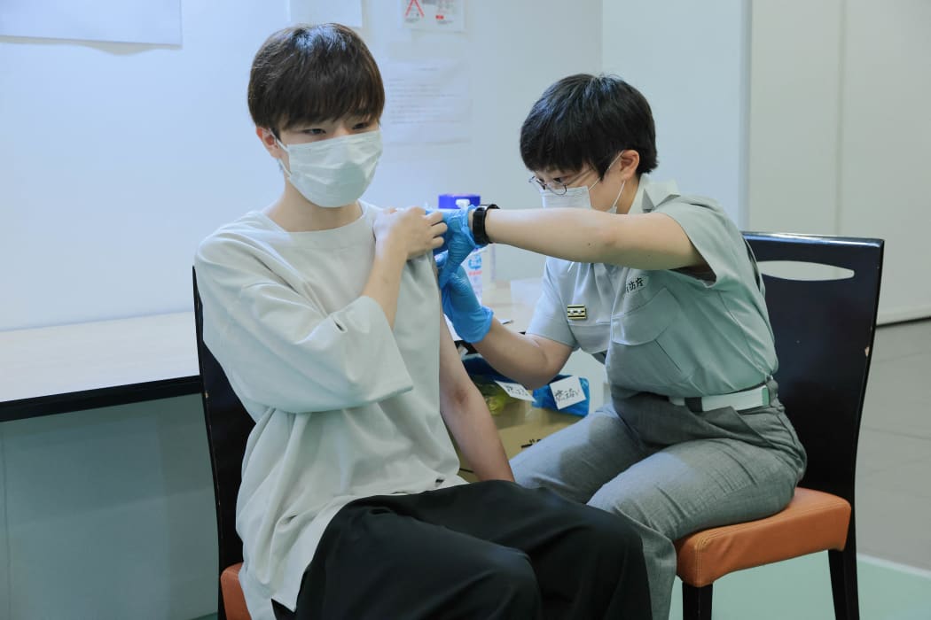 A Tokyo fire brigade staff member (R) administers a dose of the Covid-19 coronavirus vaccine at Aoyama University in Tokyo on August 2, 2021.