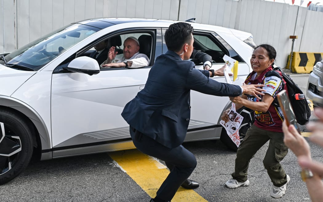 A security guard (C) stops a Catholic faithful rushing to greet Pope Francis (L) in a car as he arrives to address an interreligious meeting with young people at the Catholic Junior College in Singapore on September 13, 2024. Singapore is the last stop on the pope's 12-day, four-nation Asia-Pacific trip aimed at boosting the Catholic Church's standing in the world's most populous region. (Photo by Manan VATSYAYANA / AFP)