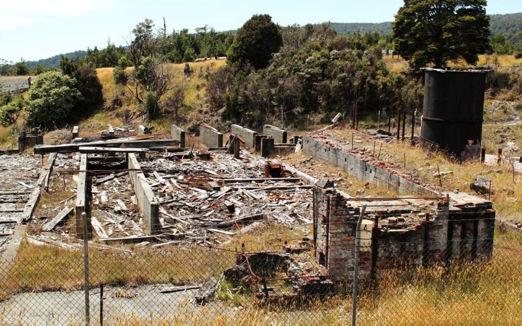 The remains of a demolished red brick building at Prohibition Mine in Waiuta, surrounded by grass and shrubs. The former mine on the West Coast is rated as the most toxic site in New Zealand