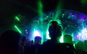 A young woman from the back dances standing in front of the stage among the crowd of festival goers. Photograph by Amaury Cornu / Hans Lucas.