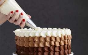 A person's hands seen piping icing on a cake.