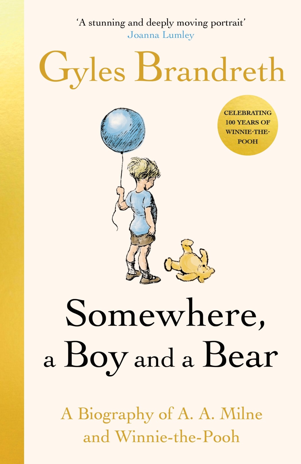 A small boy holds onto a blue balloon and looks down at his yellow toy bear at his feet