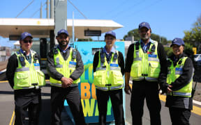 Auckland transport staff in high vis vests stand at a train station.