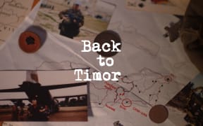 A birds'-eye view of some military items sitting scattered on a desk, including a map, a hat, playing cards, and a couple of coins. The text in the middle reads "Back to Timor."