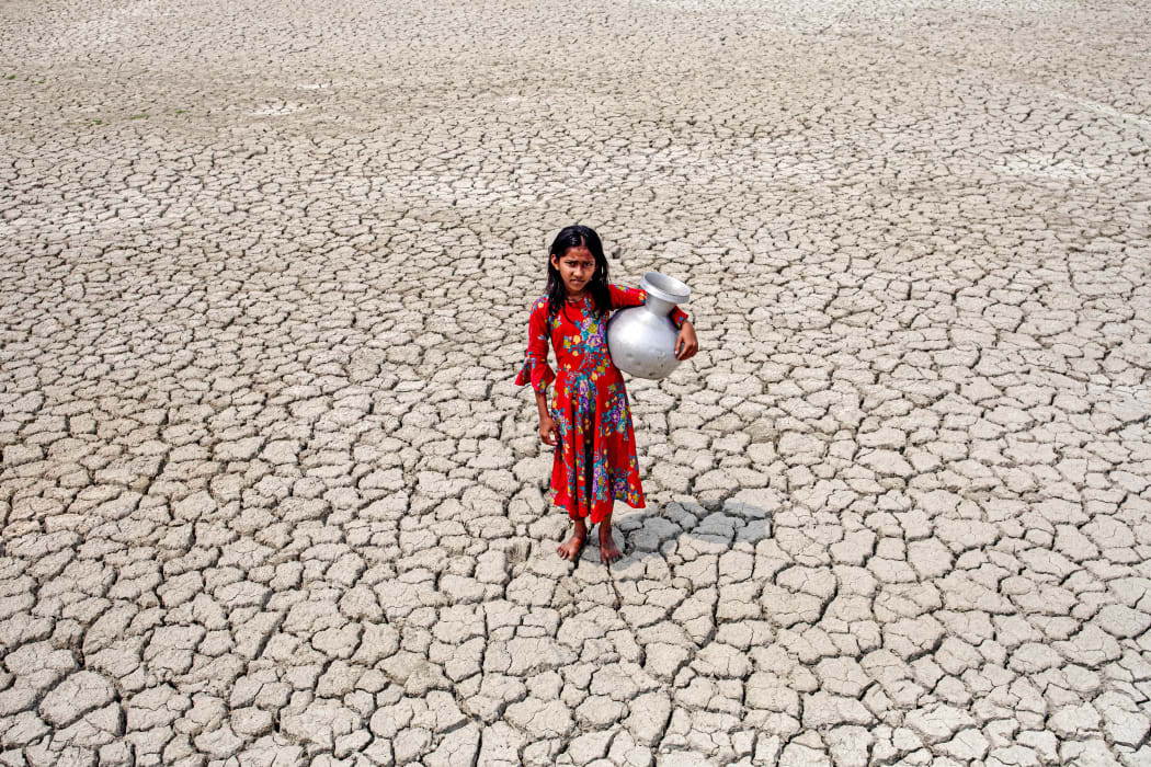 A girl walks over cracked ground after collecting drinking water from a pond near mangrove forest Sundarban in Satkhira, Bangladesh on 27 March, 2022.