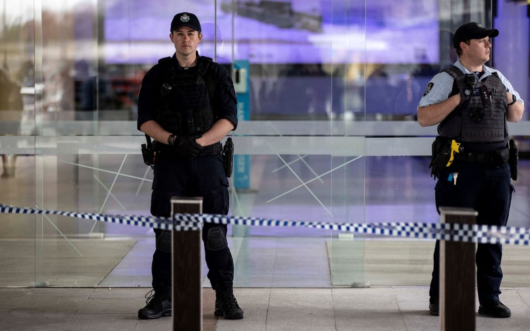 Police stand guard at the entrance of a terminal after a gunman opened fire at the airport in Canberra on August 14, 2022. - A gunman fired about five shots inside Canberra's main airport on August 14, sending passengers fleeing but injuring no-one before he was detained by Australian police. (Photo by AFP)