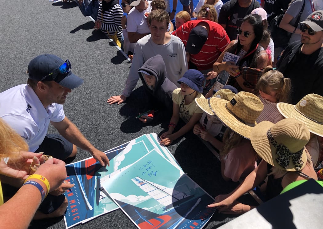 An American Magic sailor signing posters at Auckland's viaduct harbour.