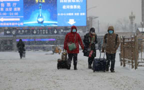 People wearing masks walk the Beijing Station area in the snow in Beijing on 6 February 2020.