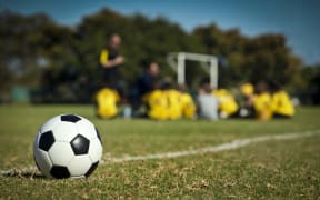 A soccer ball in the foreground, with a team of student players in the background.