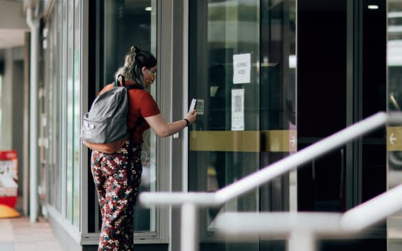 A woman using the Covid Tracer app at a QR code in the window of a business during level 2 in Wellington on15 February 2021