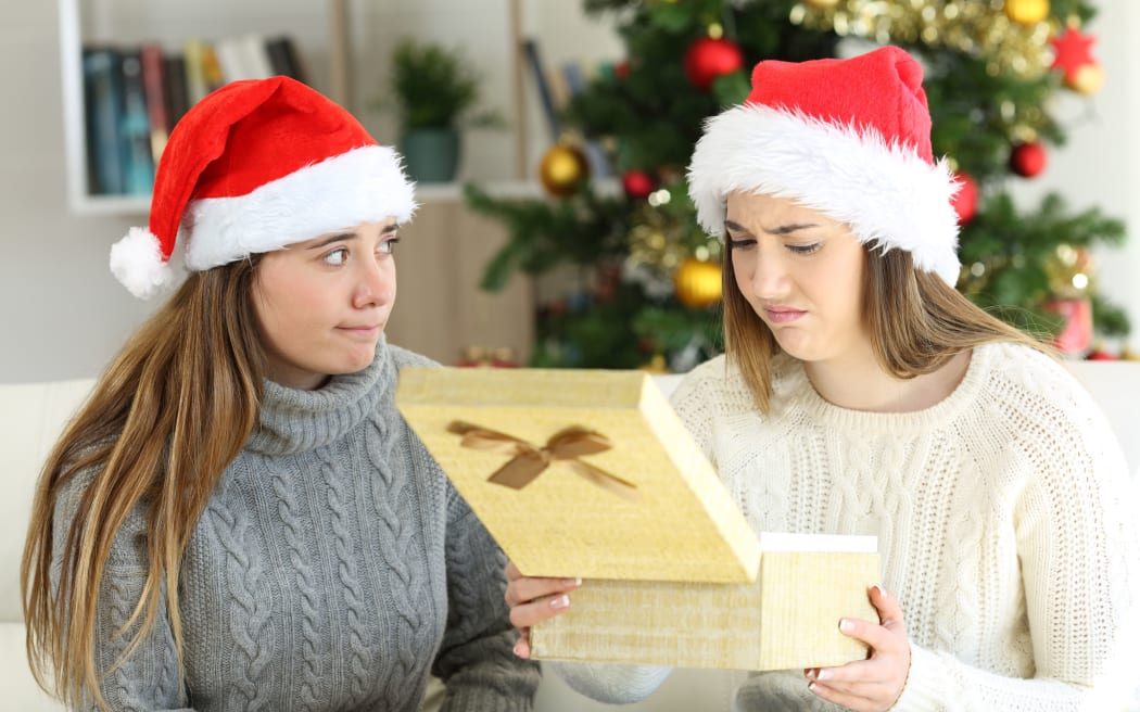 Disappointed woman receiving a gift from a friend in Christmas at home.