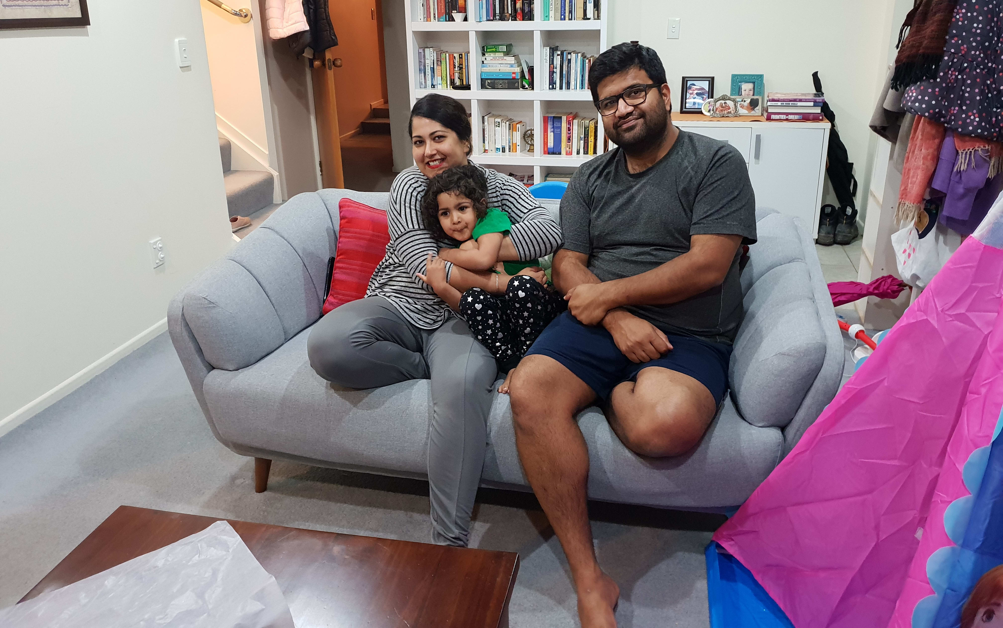 Ishita and Zorran relaxing at home on the couch with their daughter Kaya.