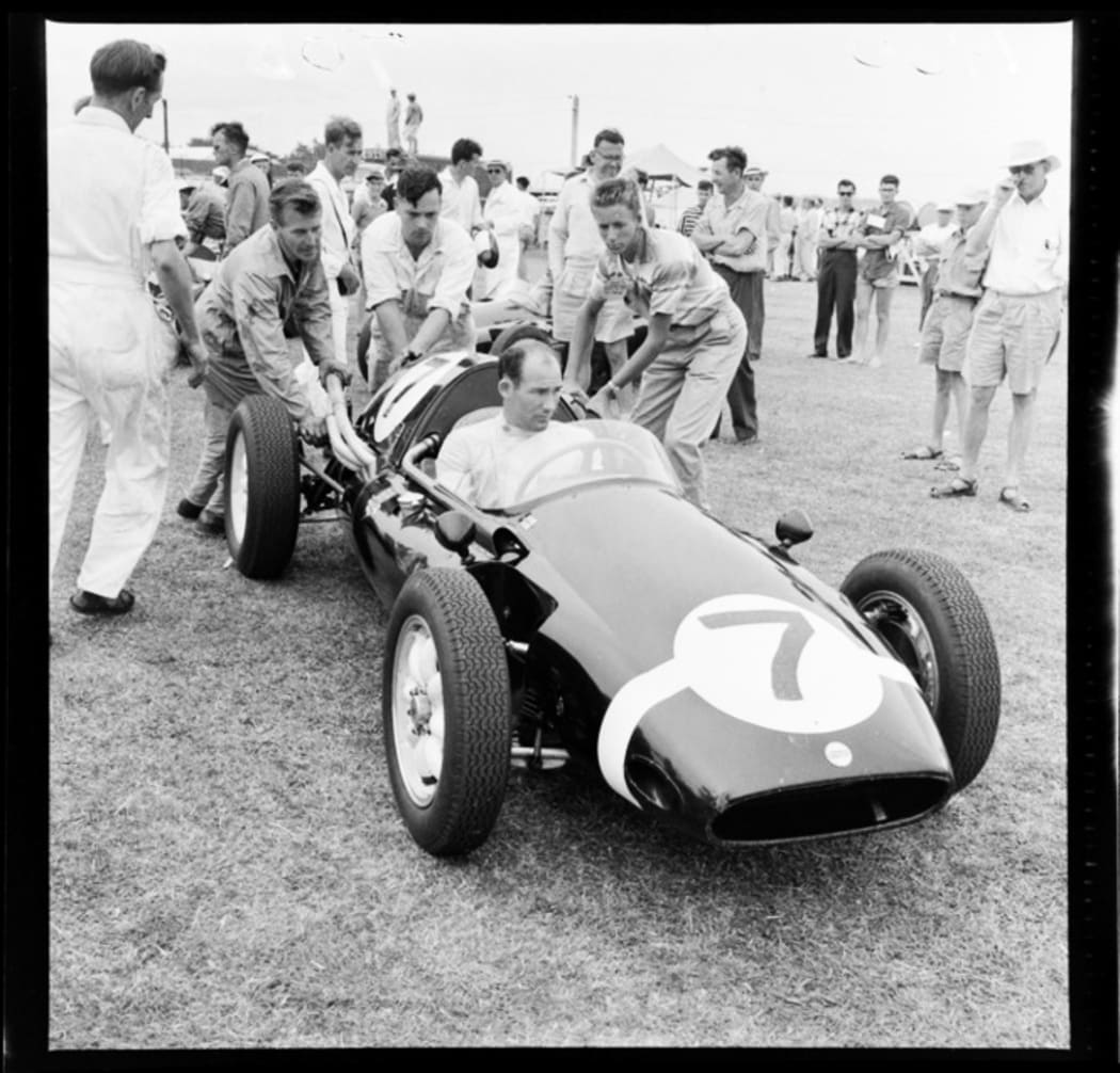 Stirling Moss in his race car No.7 being pushed by pit crew members, Ardmore Aerodrome Racetrack, South Auckland