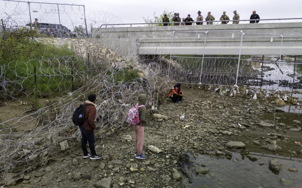 EAGLE PASS, TEXAS - MARCH 18: In an aerial view, U.S. soldiers and law enforcement officers stand over a small group of immigrants who had crossed the Rio Grande into the United States on March 18, 2024 in Eagle Pass, Texas. Texas National Guard troops have fortified the U.S.-Mexico border at Eagle Pass with vast amount of razor wire as part of Governor Greg Abbott's "Operation Lone Star" to deter migrants from crossing into Texas. The U.S. southwestern border with Mexico stretches nearly 2,000 miles, from the Gulf of Mexico to the Pacific Ocean and is marked by fences, deserts, mountains and the Rio Grande, which runs the entire length of Texas. Border and immigration issues have become dominant themes in the U.S. presidential election campaign.   John Moore/Getty Images/AFP (Photo by JOHN MOORE / GETTY IMAGES NORTH AMERICA / Getty Images via AFP)