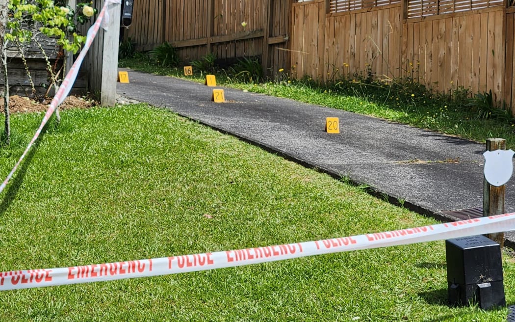 A driveway has been cordoned off by white and red police tape. It looks to be a suburban area and little yellow markers have been placed in the driveway.