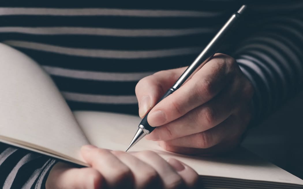Left-handed woman writing diary, close-up of hands with pencil and notebook. (Photo by IGOR STEVANOVIC / SCIENCE PHOTO / IST / Science Photo Library via AFP)