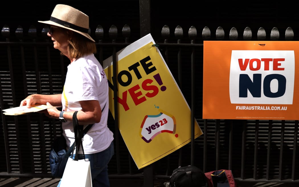 (FILES) In this photo taken on October 3, 2023, a woman handing out brochures walks past referendum promotional posters outside a voting centre in central Sydney. On October 14, 2023 almost 18 million Australians will decide whether to recognise Indigenous Australians in the constitution for the first time, and whether to create a permanent Indigenous consultative body. (Photo by DAVID GRAY / AFP) / TO GO WITH AFP STORY AUSTRALIA-INDIGENOUS-REFERENDUM-MISINFORMATION, BY JOSEPH OLBRYCHT PALMER