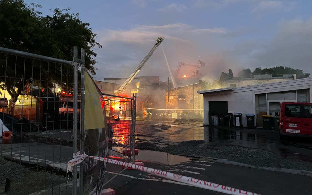 Flames could be seen over the top of a building in Onehunga Mall Road, as firefighters work from ladders, on Sunday night, 25 January, 2026.