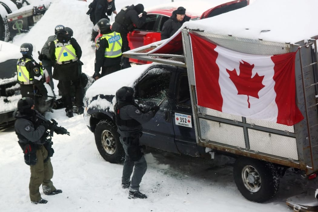 A police officer smashes a truck window as they deploy to remove protesters in Ottawa.