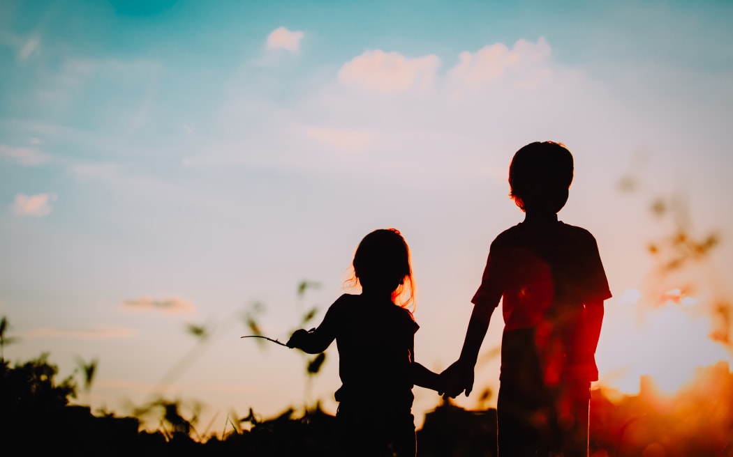 little boy and girl silhouettes holding hands at sunset nature