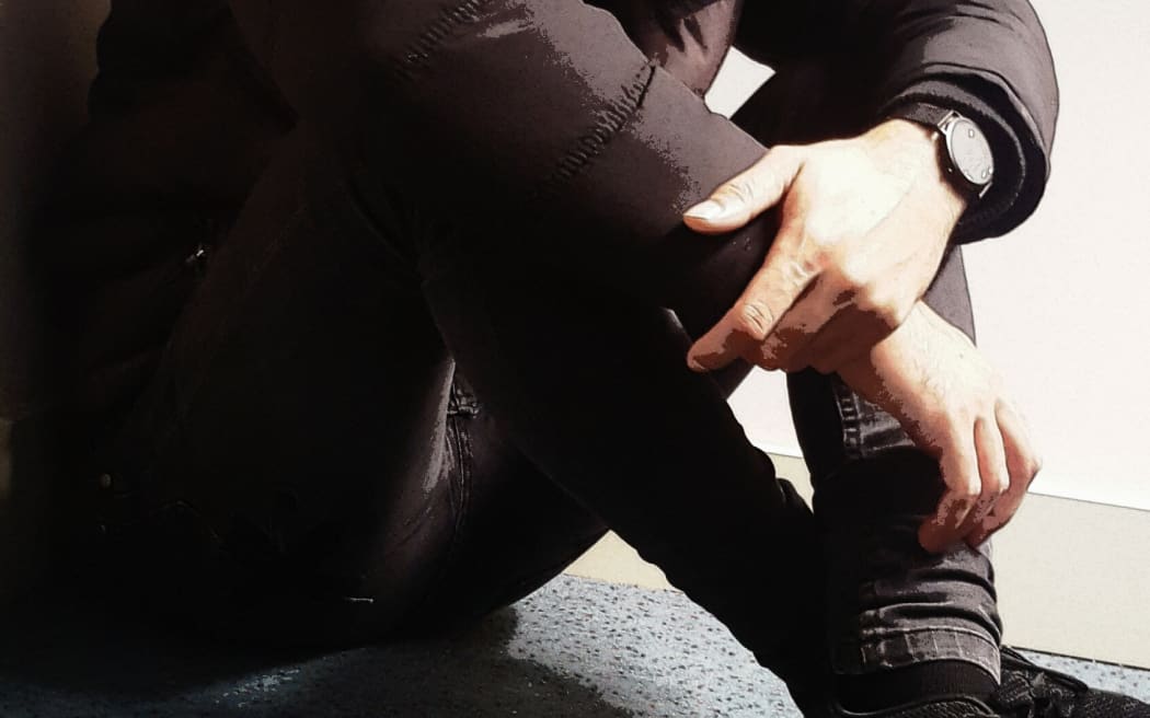 A staged photo of a young man hunched over, used to illustrate the use of seclusion rooms or mental health issues.