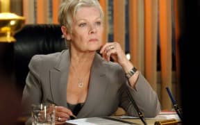 Dame Judi Dench wears a grey suit and an inscrutable look.