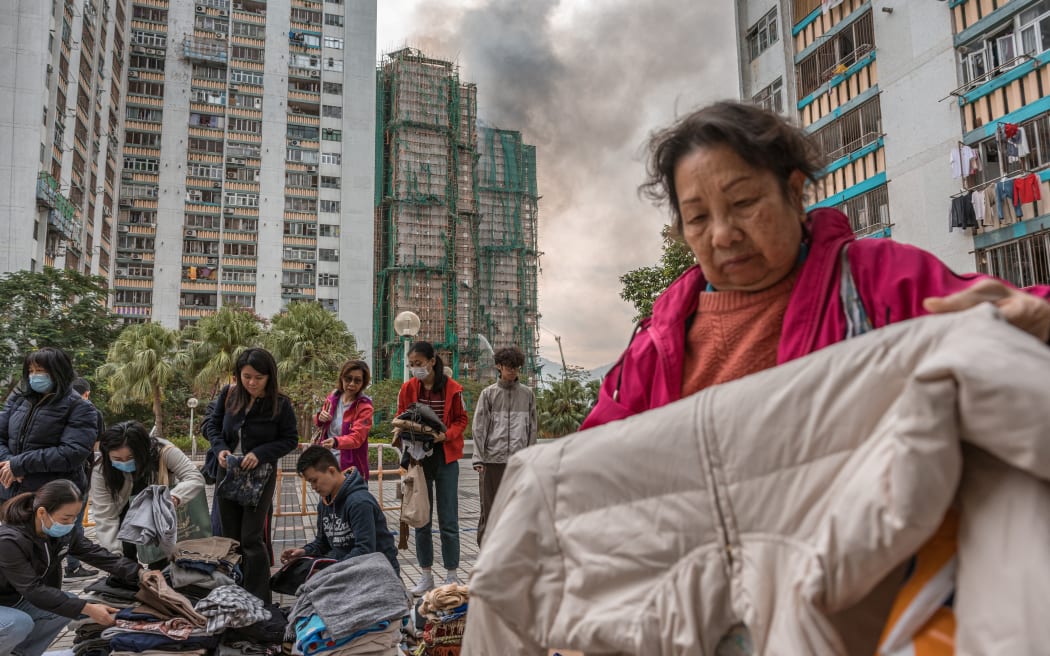 Residents check clothing donated for them after a major fire swept through several apartment blocks at the Wang Fuk Court residential estate in Hong Kong's Tai Po district on November 27, 2025. Hong Kong firefighters were scouring a still-burning apartment complex for hundreds of missing people on November 27, a day after the blaze tore through the high-rises, killing at least 44. (Photo by Dale DE LA REY / AFP)