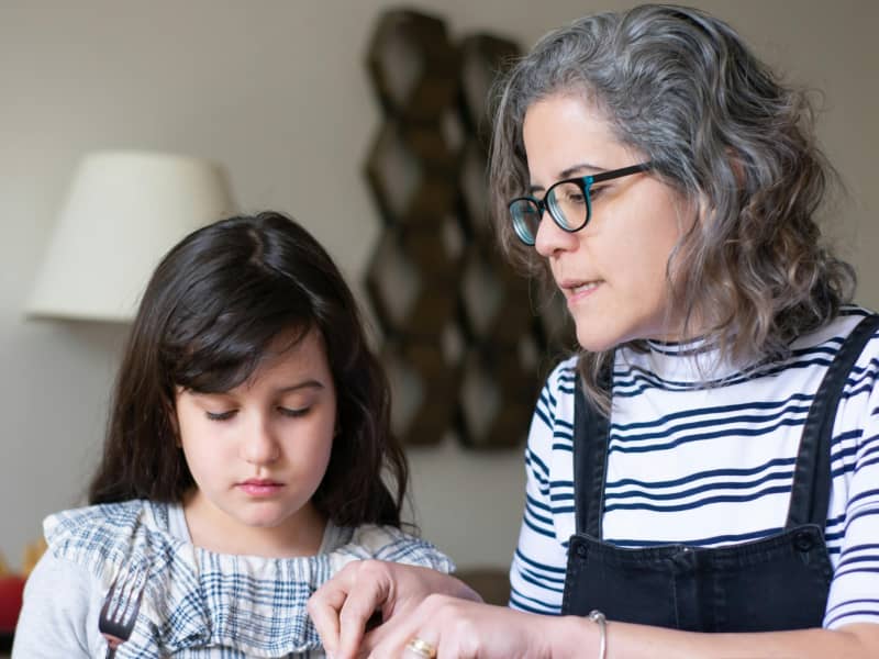 A grey-haired mother sits side by side with a dark haired girl and talks to her.