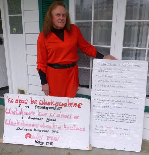 Shelley Howard outside her home holding hand made signs