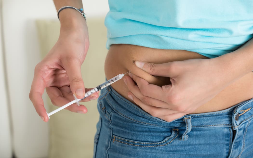 Midsection of diabetic young woman injecting stomach at home