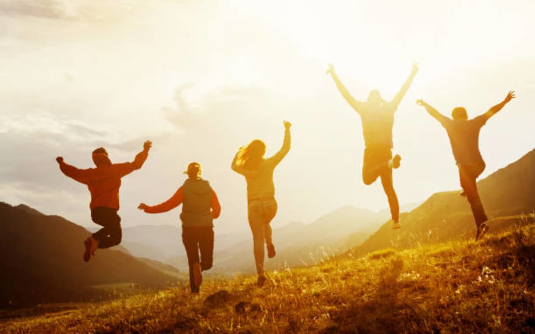 Group of five happy friends is running and jumping in sunset light on background of mountains. Happiness and friendship concept