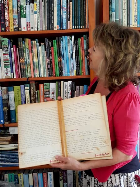 Julie Biuso looks at a bookshelf that contains some of the books she's written, as she holds the first ‘book’ she wrote when she was about 10, of handwritten family favourites. (pictured about 2010)