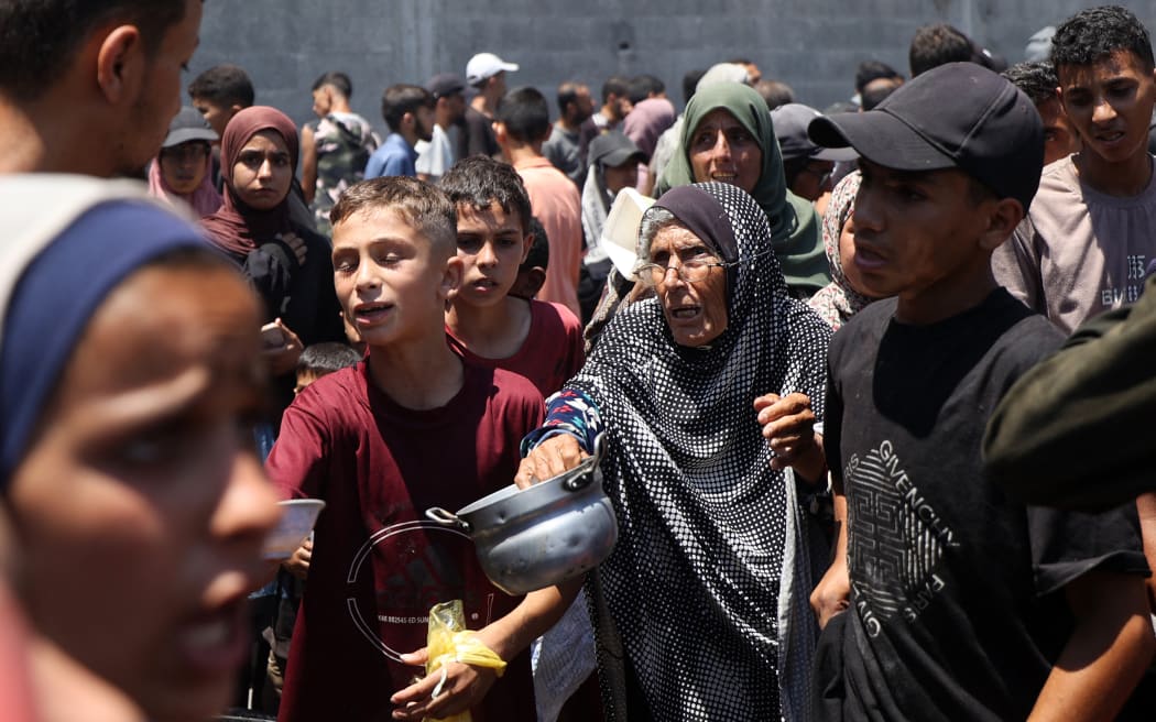 An elderly woman holds out an empty pot at a food distribution point in the Nuseirat refugee camp in the central Gaza Strip on July 19, 2025. The World Food Programme said nearly one in three people in Gaza were not eating for days at a stretch and "thousands" were "on the verge of catastrophic hunger". (Photo by Eyad BABA / AFP)