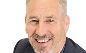 A portrait shot of Malcolm Sproull against a while backgound. He has a grey beard and the smile of a man on a self-help poster. The photo doesn't quite fit the dimensions of the website so it's a super closup of his face.