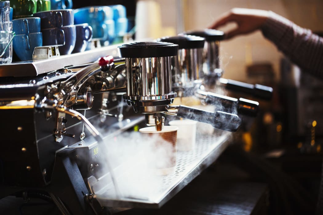 [England] Specialist coffee shop. A person working at a large coffee machine, with three percolating containers, handles and a pipe sending out steam. (Photo by Mint Images / Mint Images / Mint Images via AFP)