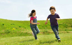 summer, childhood, leisure and people concept - happy little boy and girl playing tag game and running outdoors on green field