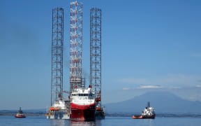 Boat and oil rig in clam sea and mountain behind