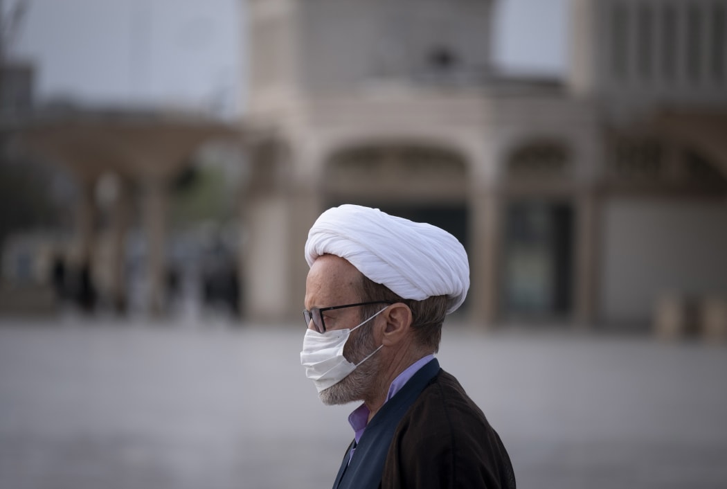 A Iranian cleric wearing a face mask walks near a shrine in the holy city of Qom, March 2020..