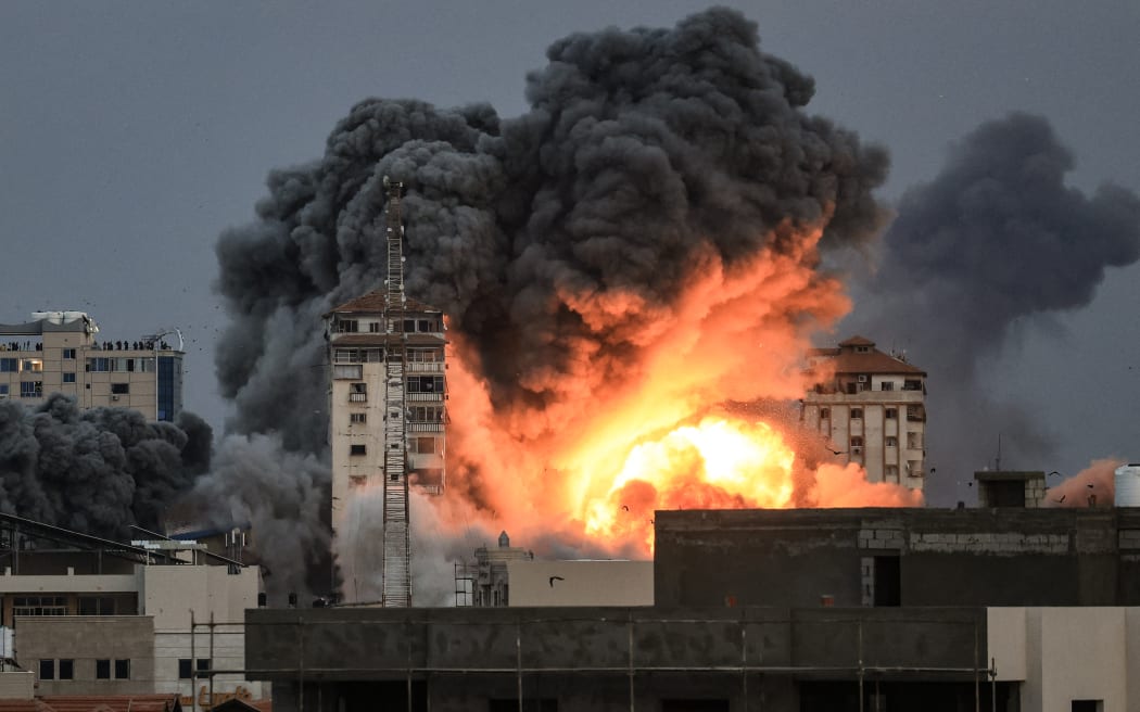 People standing on a rooftop (left), watch as a ball of fire and smoke rises above a building in Gaza City on 7 October, 2023 during an Israeli air strike.