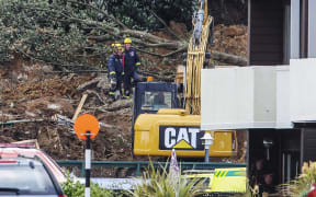 Police and officials stand following a landslide while a search is underway by local emergency services for missing people at Mount Maunganui in Tauranga on January 22, 2026. A landslide smashed into a campsite in rain-swept northern New Zealand leaving multiple people missing, police and rescuers said. (Photo by DJ MILLS / AFP)