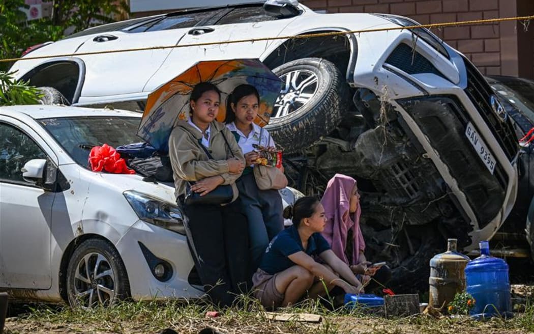 People rest beside cars, swept one on top of another by floodwaters caused by typhoon Kalmaegi, in Liloan in the province of Cebu