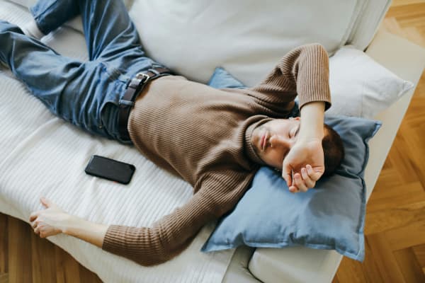 A bearded man in a brown sweater sleeps on the couch.
