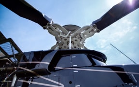 Close up of a screw of black with gray stripes bell 407 helicopter standing on green grass field in blue sky background.