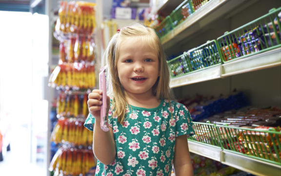 A little girl with a big smile stands next to the lolly aisle at a supermarket (file)