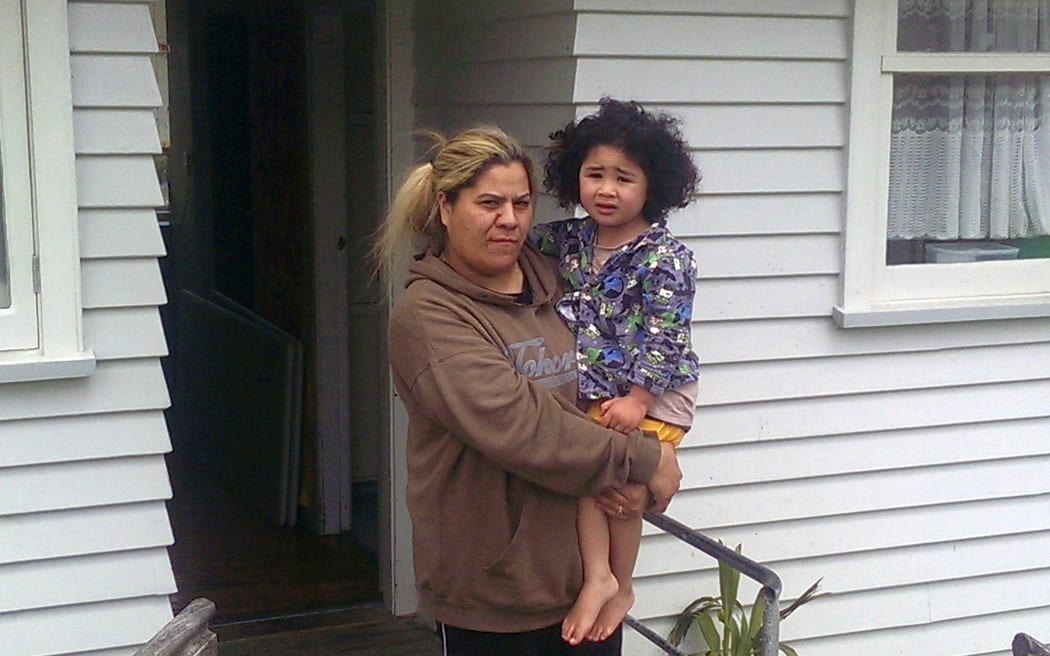 Elsie stands holding her some at the front door of their weather board home